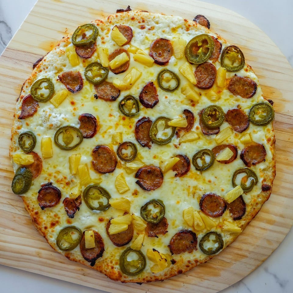 RigaTony's pizza with white sauce, sausage, pineapple, and jalapeños on a wooden peel.