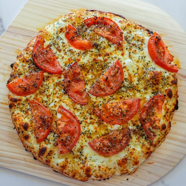 RigaTony's Pizza & Pasta's cheesy pizza with sliced tomatoes and herbs on a wooden peel.