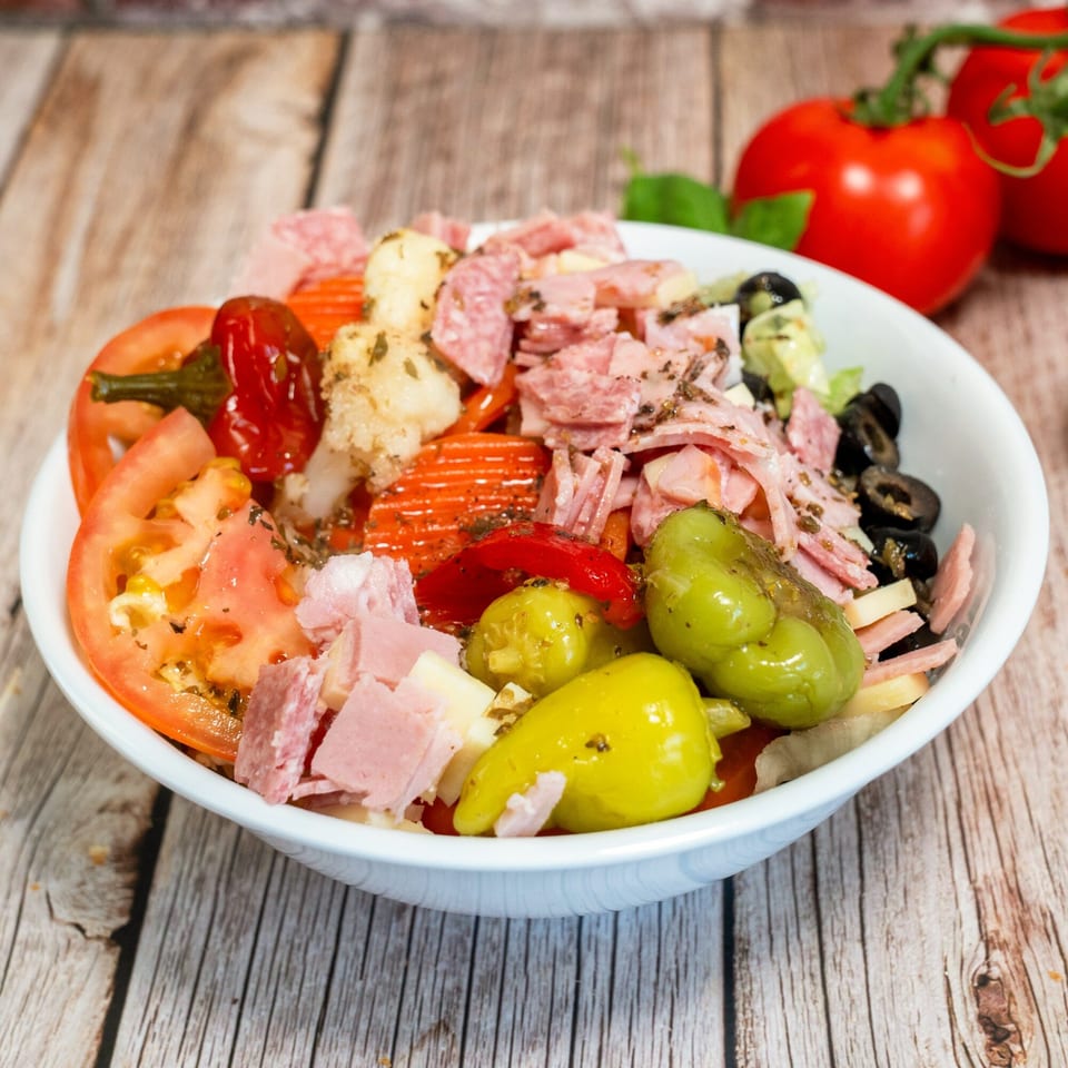 RigaTony's antipasto salad with salami, ham, cheese, tomatoes, olives, and peppers in a white bowl.