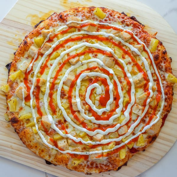 RigaTony's Buffalo Chicken Pizza with pineapple, drizzled with ranch and hot sauce in a spiral pattern.