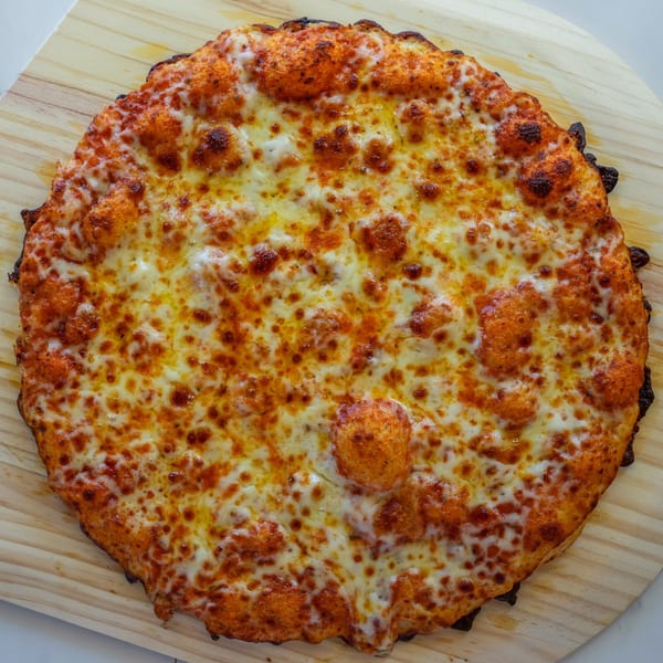 A RigaTony’s cheese pizza with bubbly, melted mozzarella and a crispy crust on a wooden peel.
