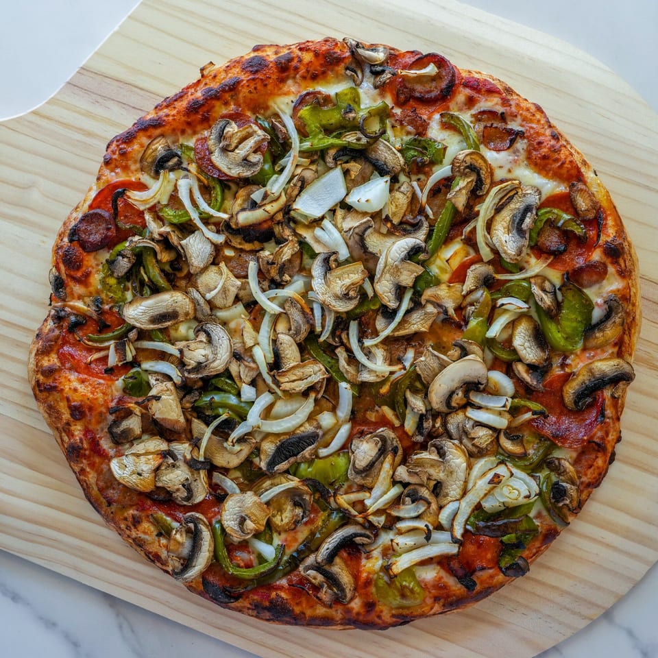 RigaTony's pizza with pepperoni, mushrooms, green peppers, and onions on a wooden peel.